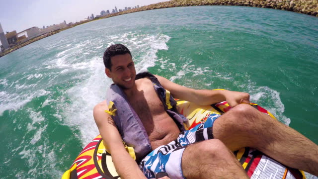 Man-sitting-in-inflatable-ring-towed-by-a-boat-in-the-water-and-recording-himself-with-Go-Pro-camera