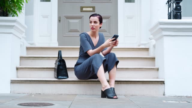 Stylish-Woman-Sitting-On-Steps-Of-Building-Using-Mobile-Phone