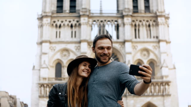 Pie-feliz-pareja-joven-cerca-de-Notre-Dame-en-París.-Francia-y-tomar-fotos-selfie-en-smartphone