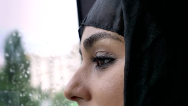 Junge-muslimische-Frau-in-Hijab-Augen-beobachtet-im-verregneten-Fenster-im-Bus,-Wetter-Konzept,-Transportkonzept,-städtebauliche-Konzept-Konzept-träumen,-Seitenansicht