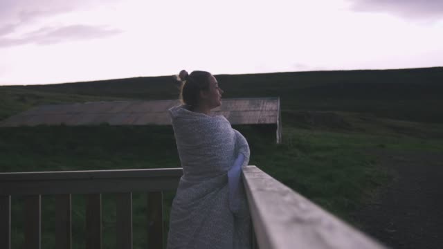 Young-woman-in-blanket-standing-on-the-balcony-enjoying-view-of-dramatic-clouds,-close-up-shot