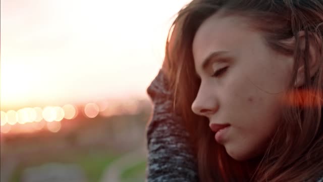 Close-up-face-of-young-pensive-woman-melancholically-looking-at-amazing-sunset-and-touching-hair