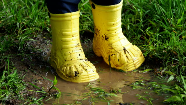 Kleines-Kind-in-leuchtend-gelben-Latex-Stiefel-in-einer-Pfütze-planschen.-Kid-es-Füße-geschützt-von-Schmutzwasser