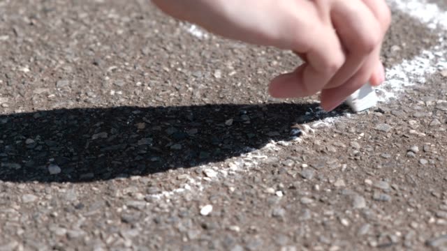 Woman-draws-a-line-on-the-asphalt-with-white-chalk.-Close-up-hand.