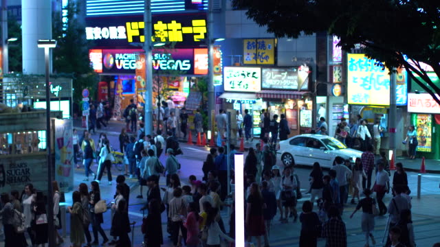 MATERIAL-EDITORIAL:-Movimiento-tiro-alto-ángulo-de-la-concurrida-calle-grande-de-la-ciudad-con-multitud-de-personas-caminando-en-la-noche.-Carteles-de-publicidad-que-brilla-intensamente.-Tokio-de-noche.