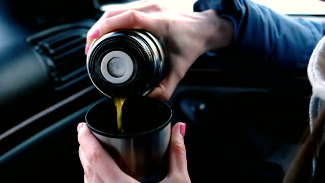 Close-up-woman's-hands-pouring-a-hot-tea-in-a-cup-from-thermos-in-the-car-in-winter.