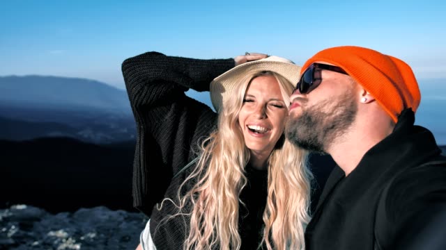 Pov-shot-traveler-couple-in-hat-posing-smiling-sending-air-kiss-and-pulling-face-taking-selfie