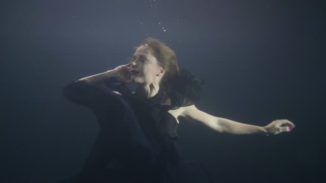 Mysterious-woman-in-black-dress-swimming-like-mermaid-under-water-in-dark-pool