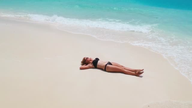 Wunderschöne-Frau-sonnt-sich-auf-Sand-Zunge-umgeben-von-türkisblauem-Wasser