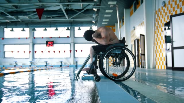 Disabled-man-in-a-wheelchair-putting-on-a-swimming-cap-and-a-goggles.-Side-angle