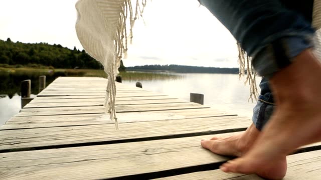 Close-up-on-woman's-feet-standing-on-jetty-above-lake