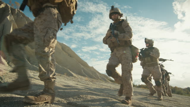 Escuadrón-de-soldados-armados-y-totalmente-equipados-caminando-en-un-solo-archivo-en-el-desierto.-Cámara-lenta.