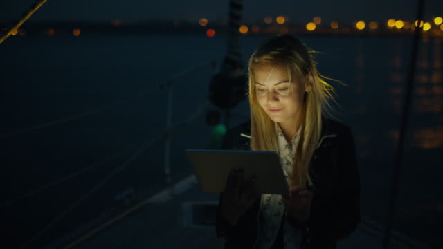 Mädchen-nutzt-nachts-eine-Tablette-auf-einem-Segelboot-im-Meer.