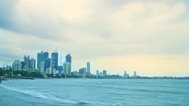 Evening-time-lapse-shot-of-the-clouds-passing-over-the-city-buildings-(city-skyline)-most-of-them-are-under-construction-while-Arabian-sea-in-the-foreground,-Mumbai,-India