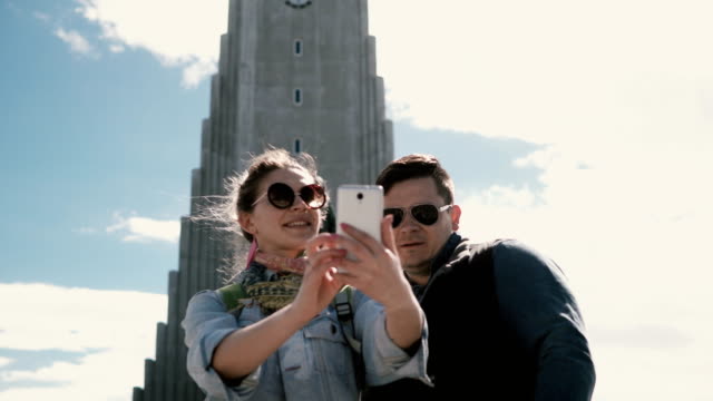 Joven-pareja-feliz-tomando-la-foto-selfie-en-teléfono-inteligente-cerca-de-la-iglesia-de-Hallgrímskirkja-en-Reykjavik,-Islandia