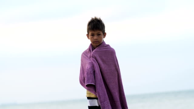 tired-sad-refugee-boy-in-a-towel-stands-alone-looking-into-the-camera,-boy-is-trying-to-keep-warm