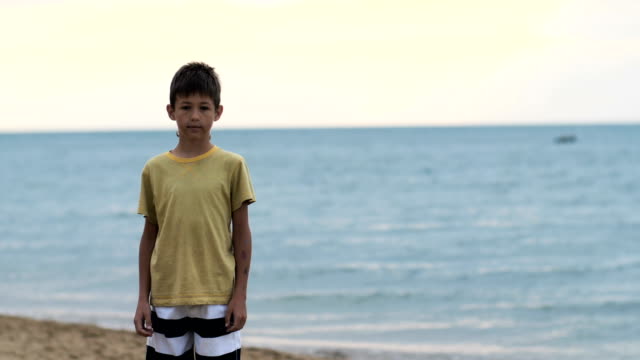 boy-stands-on-the-beach-near-the-sea-and-looks-at-the-camera