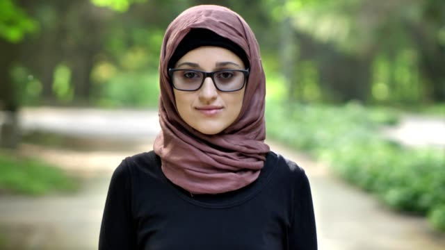 Retrato-de-una-joven-de-gafas-usar-hijab,-al-aire-libre,-en-un-parque-en-el-fondo.-50-fps