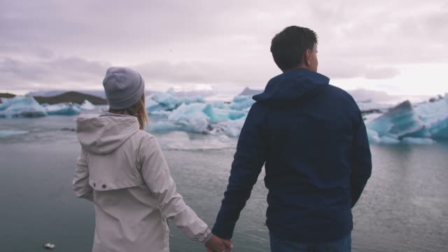 Young-couple-looking-at-Jokulsarlon-glacier-lake-in-Iceland,-cinematic-shot