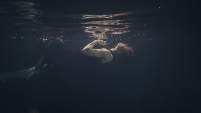 Fashion-model-in-black-dress-swimming-underwater-on-dark-background