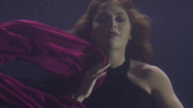 Mysterious-woman-in-chiffon-dress-swimming-underwater-pool-on-dark-background.