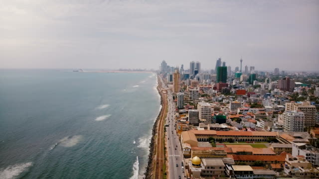 Impresionante-vista-aérea-de-Colombo,-Sri-Lanka.-Drone-volando-sobre-calle-concurrida-de-la-ciudad,-las-olas-del-océano-y-la-arquitectura-asiática-moderna