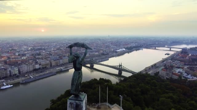 Vuelo-alrededor-de-la-estatua-de-la-libertad-con-el-horizonte-de-Budapest-en-el-fondo.-Budapest,-Hungría---imágenes-aéreas-de-4K-al-amanecer