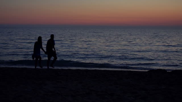 Pareja-de-enamorados-caminando-por-la-orilla-del-mar-al-atardecer,-romántico-paseo