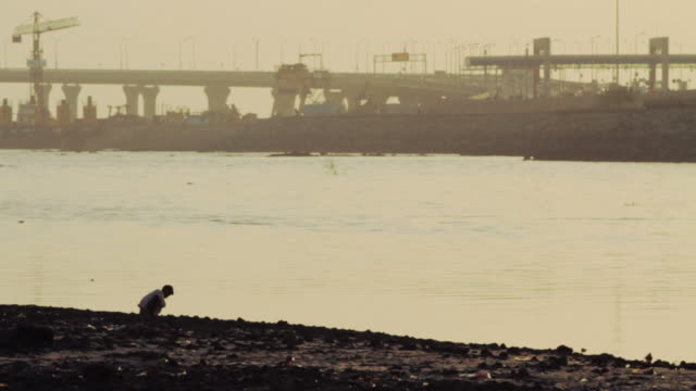 Kind-sitzt-auf-dem-Fluss-Strand-in-Mumbai.