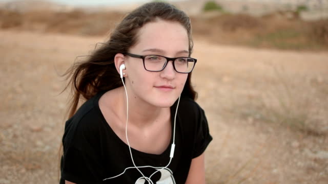 Teenage-girl-with-glases-sitting-on-the-ground-listening-to-the-music-outdoor