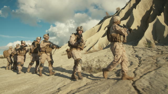 Kader-von-voll-ausgestatteten-und-bewaffneten-Soldaten-laufen-im-Gänsemarsch-in-der-Wüste.