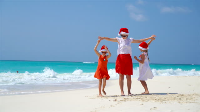 Kleine-Mädchen-und-junge-Mutter-in-Santa-Hüte-am-Strand-Weihnachtsferien