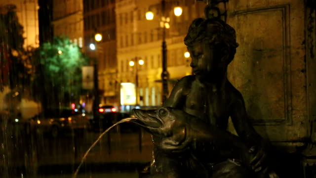 Statue-der-Junge-sitzt-am-Brunnen-halten-Fische-in-der-Nacht,-Pfanne,-Romantik