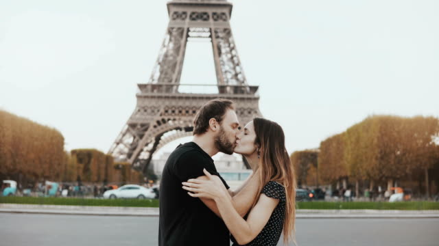 Young-happy-couple-walking,-kissing-near-the-Eiffel-tower-in-Paris,-France.-Traveling-man-and-woman-on-honeymoon