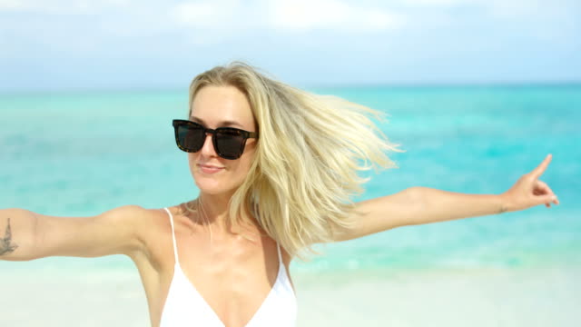 Portrait-of-the-Beautiful-Blonde-Woman-Wearing-Sunglasses-Posing-and-Smiling-on-the-Beach.-In-the-Background-Sea-Resort.