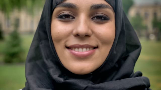 Gesicht-des-jungen-Sencere-muslimisches-Mädchen-Hijab-ist-tagsüber-bei-schlechtem-Wetter,-gerade-in-die-Kamera,-Religiuos-Konzept,-der-Hintergrund-jedoch-unscharf-lächelnd.