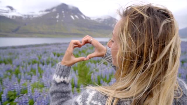 Mujer-joven-de-pie-en-el-Prado-de-flores-púrpura-lupine-en-Islandia-haciendo-marco-del-dedo-corazón-forma