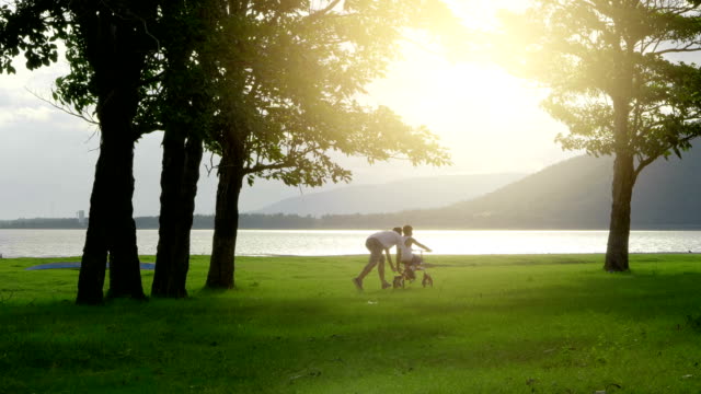 Práctica-asiática-hijo-a-montar-en-bicicleta-con-su-padre,-Feliz-familia-en-el-Parque-natura,-el-movimiento-lento-de-vídeo-de-4-K