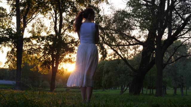 Mujer-en-vestido-blanco-disfrutar-la-puesta-de-sol-en-el-parque,-vista-parte-trasera