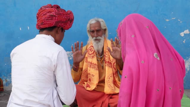 In-Rosa-Sari-Brautpaar-in-weißem-Kurta-und-roten-Turban-suchen-Segen-aus-einer-alten-hinduistischen-Sadhu-in-Safran-frisch-vermählte-Ehemann-Ehefrau