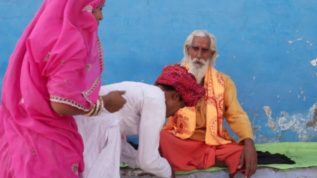 Couple-husband-wife-in-pink-and-white-and-red-turban-seek-blessings-from-a-Hindu-priest-in-Pushkar,-Rajasthan
