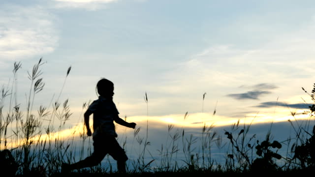 Niño-dos-7-años-feliz-con-un-funcionamiento-y-saltar-en-el-Prado-en-verano-en-la-naturaleza-el-tiempo-de-puesta-de-sol.-Movimiento-lento-de-vídeo-de-4-K