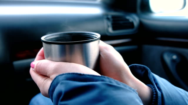 Detailansicht-von-Frauenhand-eine-Tasse-heißen-Tee-aus-der-Thermoskanne-sitzen-im-Auto-im-Winter-zu-halten.