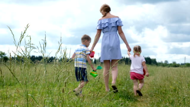 Young-mother-with-two-young-children-walking-in-the-field-on-the-grass-in-summer.-Happy-family-on-a-walk.
