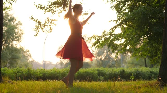 Happy-woman-in-red-transparent-dress-spinning-around-against-sunset