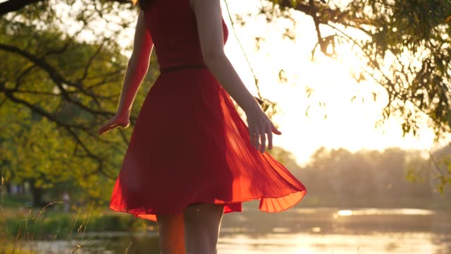 Figura-de-mujer-en-vestido-rojo-transparente-bailando-y-girando-alrededor-contra-lago-al-atardecer