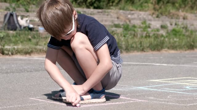 Boy-is-drawing-hopscotch-on-the-asphalt.-Close-up-view.