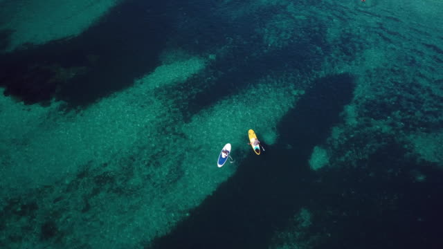 Video-from-above,-aerial-view-of--two-people-on-a-stand-up-paddle-(SUP)-in-Sardinia,-Italy.