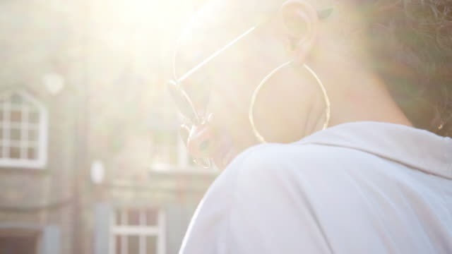 Fashionable-young-black-woman-wearing-sunglasses-talking-on-the-street,-close-up,-side-view,-lens-flare