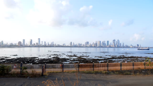 Cyclists-and-people-on-narrow-sidewalk-near-Mumbai-Worli-sea-link-skyline.